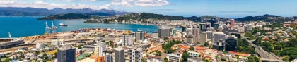 Aerial view of Wellington, New Zealand, showcasing the city skyline, harbor, and surrounding hills under a bright blue sky