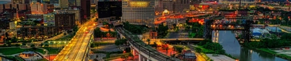 Nighttime aerial view of the Cleveland skyline with illuminated buildings, roads, and bridges reflecting on the Cuyahoga River