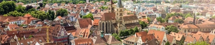 Aerial view of Stuttgart, Germany, featuring historic buildings, vineyards, and green hills under a partly cloudy sky