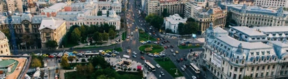 Aerial view of a bustling cityscape with a prominent intersection in Bucharest, heavy traffic, historic and modern buildings, green park with a statue, and partly cloudy sky