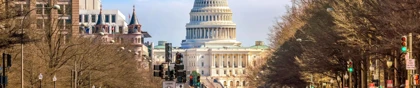 View of the U.S. Capitol building from a busy street in Washington, D.C., lined with trees and cars
