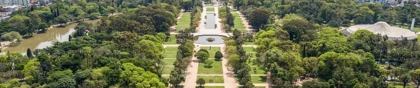 Aerial view of Redemption Park (Parque Farroupilha) in Porto Alegre, Brazil, with green trees, pathways, and a city skyline in the background.