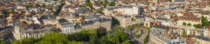 Aerial view of Dijon, France, showcasing historic architecture, green spaces, and urban layout under a blue sky